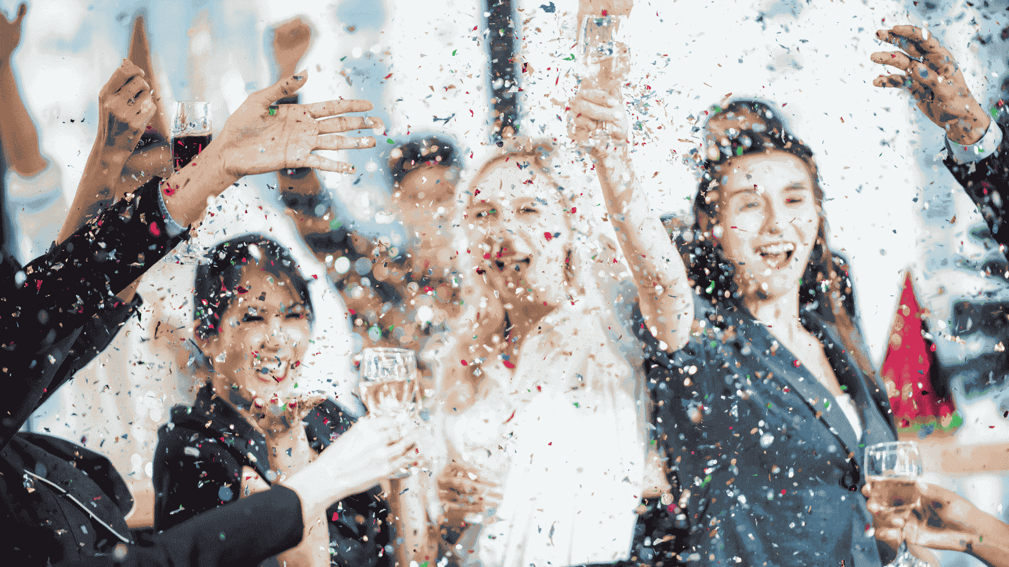 A party of people holding wine glasses cheer while confetti falls around them.